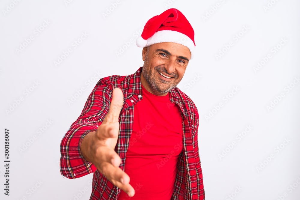 Middle age man wearing Christmas Santa hat standing over isolated white background smiling friendly offering handshake as greeting and welcoming. Successful business. Middle age man wearing Christmas Santa hat standing over isolated white background smiling friendly offering handshake as greeting and welcoming. Successful business.