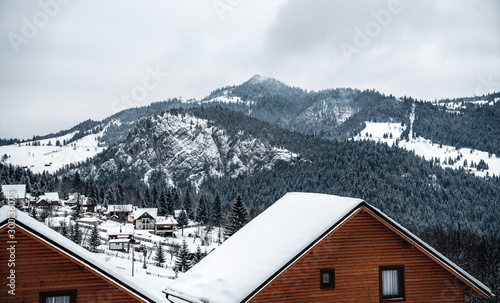 Winter houses on winter mountain landscape with white snowy spruces. Amazing view on snowcovered forested mountain slope. Christmas holiday concept. Carpathian mountains, Europe