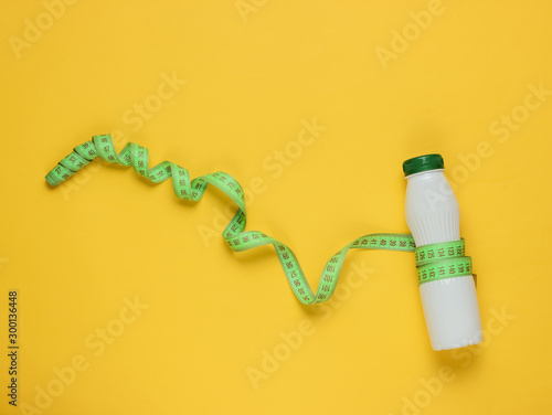 Minimalistic diet concept. Kefir bottle, measuring tape on yellow background. Top view