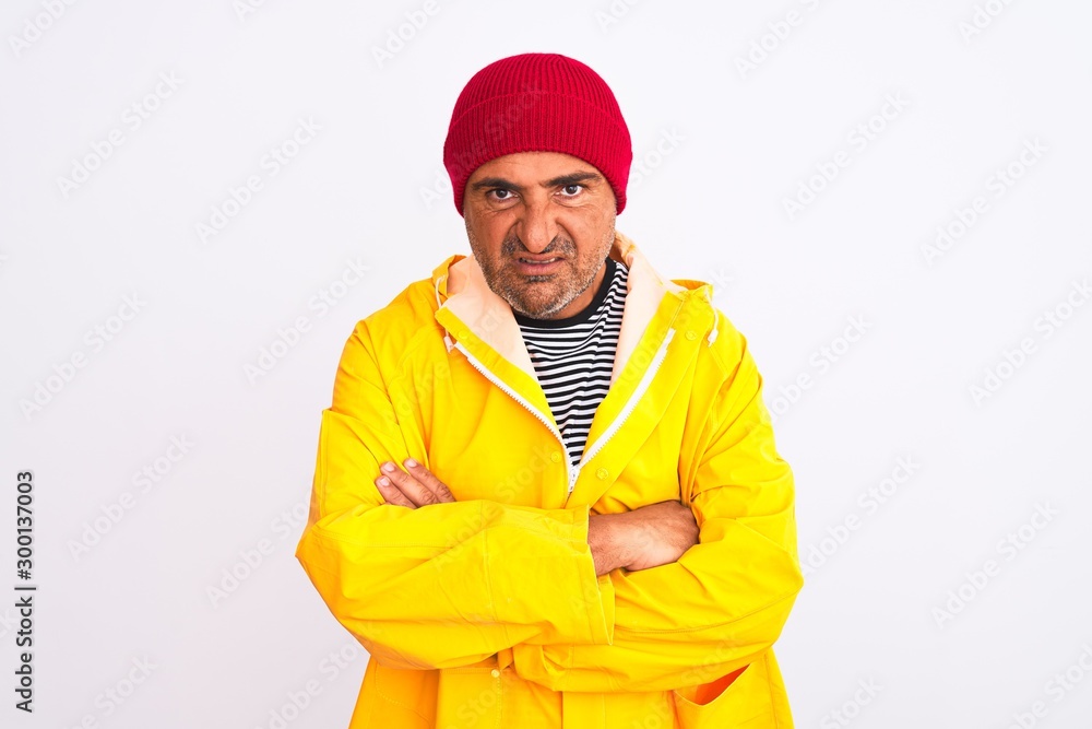 Middle age man wearing rain coat and woolen hat standing over isolated white background skeptic and nervous, disapproving expression on face with crossed arms. Negative person. Middle age man wearing rain coat and woolen hat standing over isolated white background skeptic and nervous, disapproving expression on face with crossed arms. Negative person.