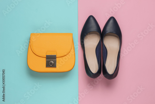 Minimalistic fashion still life. Classic women’s high heel shoes, yellow leather bag on pink background.