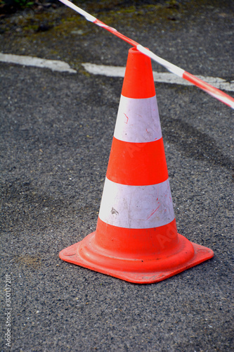 close-up on an orange white traffic cone with red-white caution tape at a street construction site, traffic cone on street for people safety
