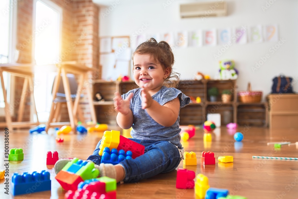Beautiful toddler sitting on the floor playing with building blocks toys at kindergarten Beautiful toddler sitting on the floor playing with building blocks toys at kindergarten