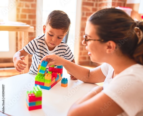 Beautiful teacher and toddler boy playing with construction blocks bulding tower at kindergarten