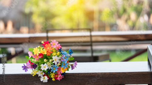 Variety of colorful plastic flowers on a wooden table blurred background