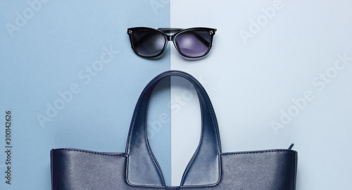 Leather bag, sunglasses on gray-blue background. Top view