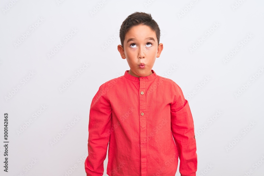Beautiful kid boy wearing elegant red shirt standing over isolated white background making fish face with lips, crazy and comical gesture. Funny expression. Beautiful kid boy wearing elegant red shirt standing over isolated white background making fish face with lips, crazy and comical gesture. Funny expression.