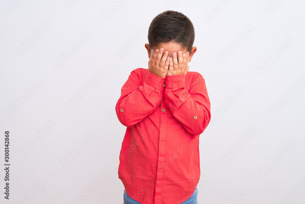 Beautiful kid boy wearing elegant red shirt standing over isolated white background with sad expression covering face with hands while crying. Depression concept. Beautiful kid boy wearing elegant red shirt standing over isolated white background with sad expression covering face with hands while crying. Depression concept.
