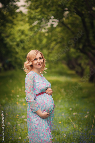 Pregnant happy Woman touching her belly. Pregnant middle aged mother portrait, caressing her belly and smiling close-up. Healthy Pregnancy concept, brunette expectant female on the park