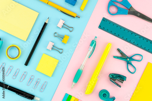 Yellow and blue stationery on a blue and pink pastel geometric background. Square school concept flat lay