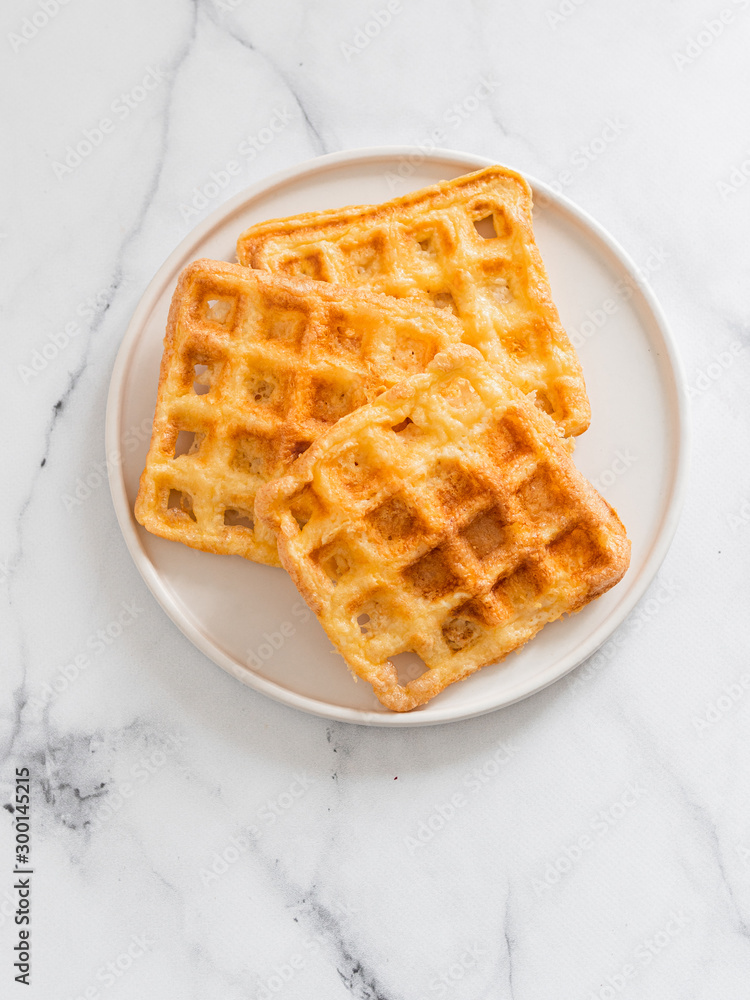 Perfect savory keto waffles. Two ingredients chaffles on plate over white marble background. Eggs and parmesan cheese low carb waffles. Top view or flat lay. Copy space for text or design. Vertical. Perfect savory keto waffles. Two ingredients chaffles on plate over white marble background. Eggs and parmesan cheese low carb waffles. Top view or flat lay. Copy space for text or design. Vertical.