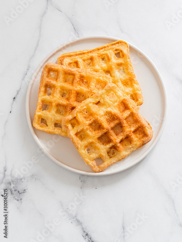 Perfect savory keto waffles. Two ingredients chaffles on plate over white marble background. Eggs and parmesan cheese low carb waffles. Top view or flat lay. Copy space for text or design. Vertical.
