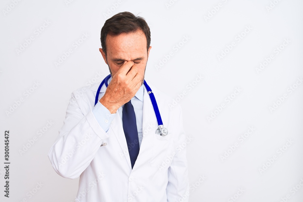 Middle age doctor man wearing coat and stethoscope standing over isolated white background tired rubbing nose and eyes feeling fatigue and headache. Stress and frustration concept. Middle age doctor man wearing coat and stethoscope standing over isolated white background tired rubbing nose and eyes feeling fatigue and headache. Stress and frustration concept.