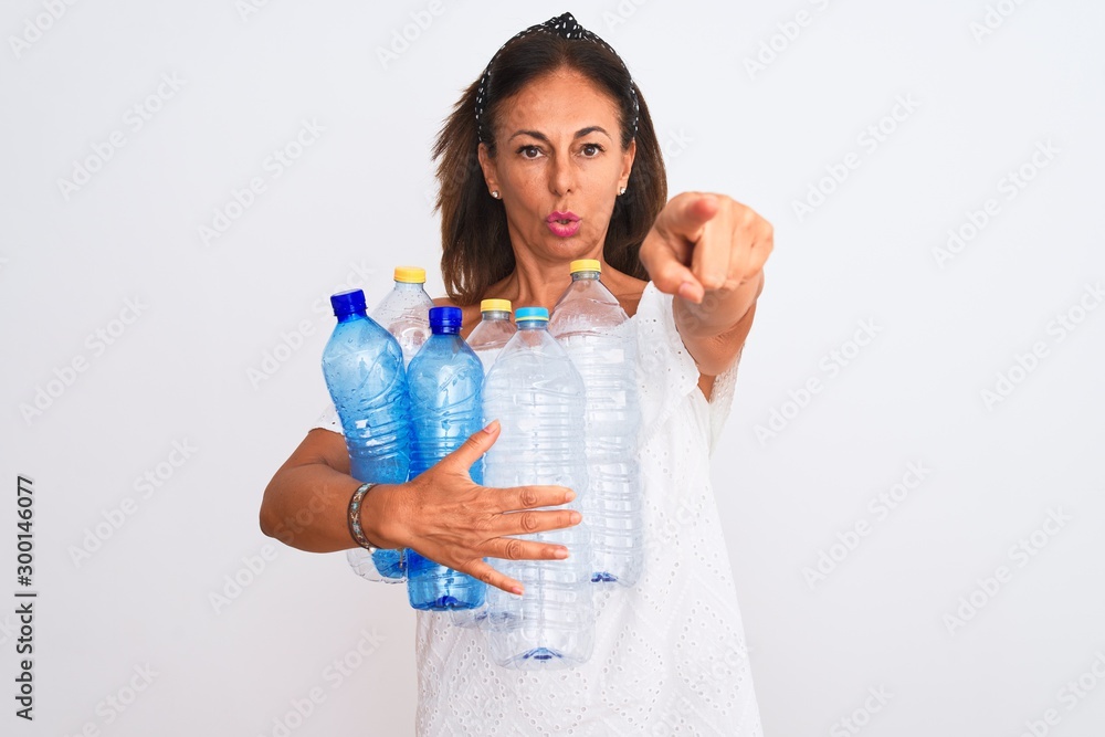 Middle age beautiful woman recycling plastic bottles standing over isolated white background pointing with finger to the camera and to you, hand sign, positive and confident gesture