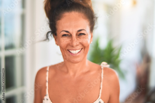 Middle age beautiful woman standing on terrace with plants smiling