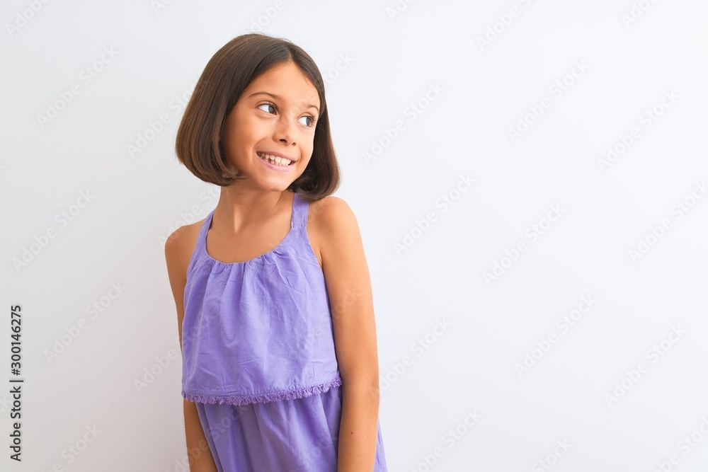Young beautiful child girl wearing purple casual dress standing over isolated white background looking away to side with smile on face, natural expression. Laughing confident. Young beautiful child girl wearing purple casual dress standing over isolated white background looking away to side with smile on face, natural expression. Laughing confident.