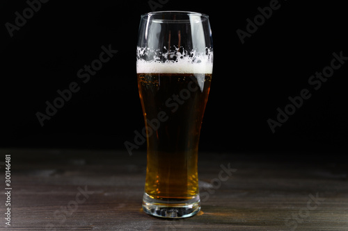Photo of beer in a glass. Thick foam and a nice color drink on a black background.
