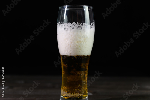 Photo of beer in a glass. Thick foam and a nice color drink on a black background.