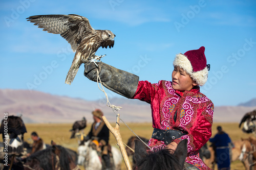 Fotografie Young Mongolian boy in traditional Mongolian dress holding his falcon on horseback