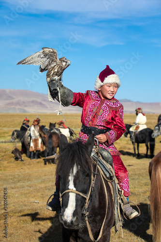 Fotografie Young Mongolian boy in traditional Mongolian dress holding his falcon on horseback