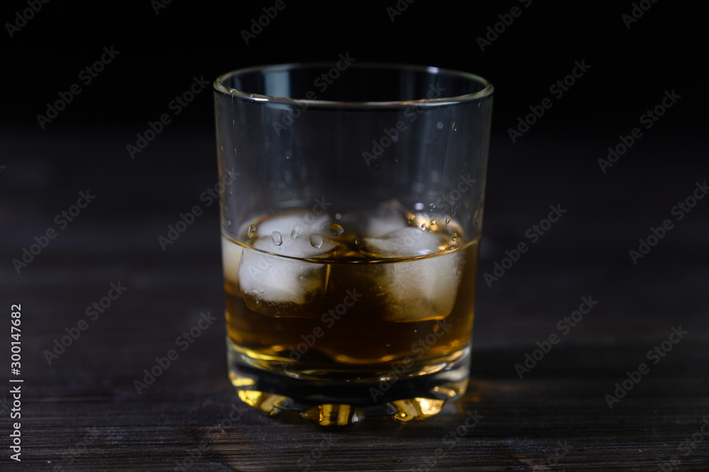 Photo of whiskey in a glass with ice. Real ice and a pleasant color of the drink on a black background.