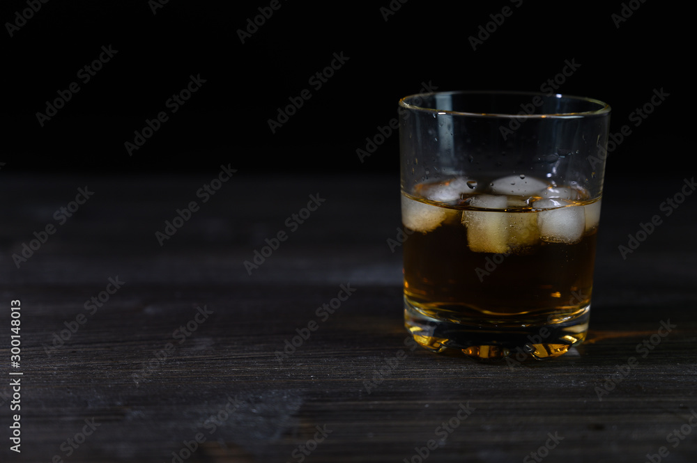 Photo of whiskey in a glass with ice. Real ice and a pleasant color of the drink on a black background. Photo of whiskey in a glass with ice. Real ice and a pleasant color of the drink on a black background.