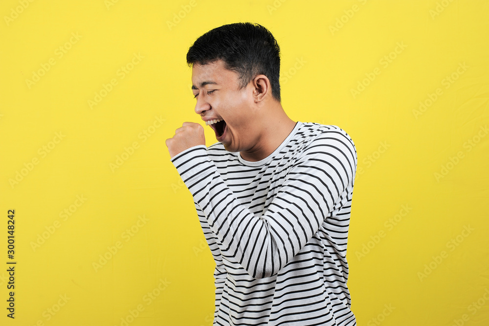 Portrait of funny Asian man yawning covering open mouth and showing a sleepy gesture. feeling being tired from hard work, isolated on yellow Portrait of funny Asian man yawning covering open mouth and showing a sleepy gesture. feeling being tired from hard work, isolated on yellow