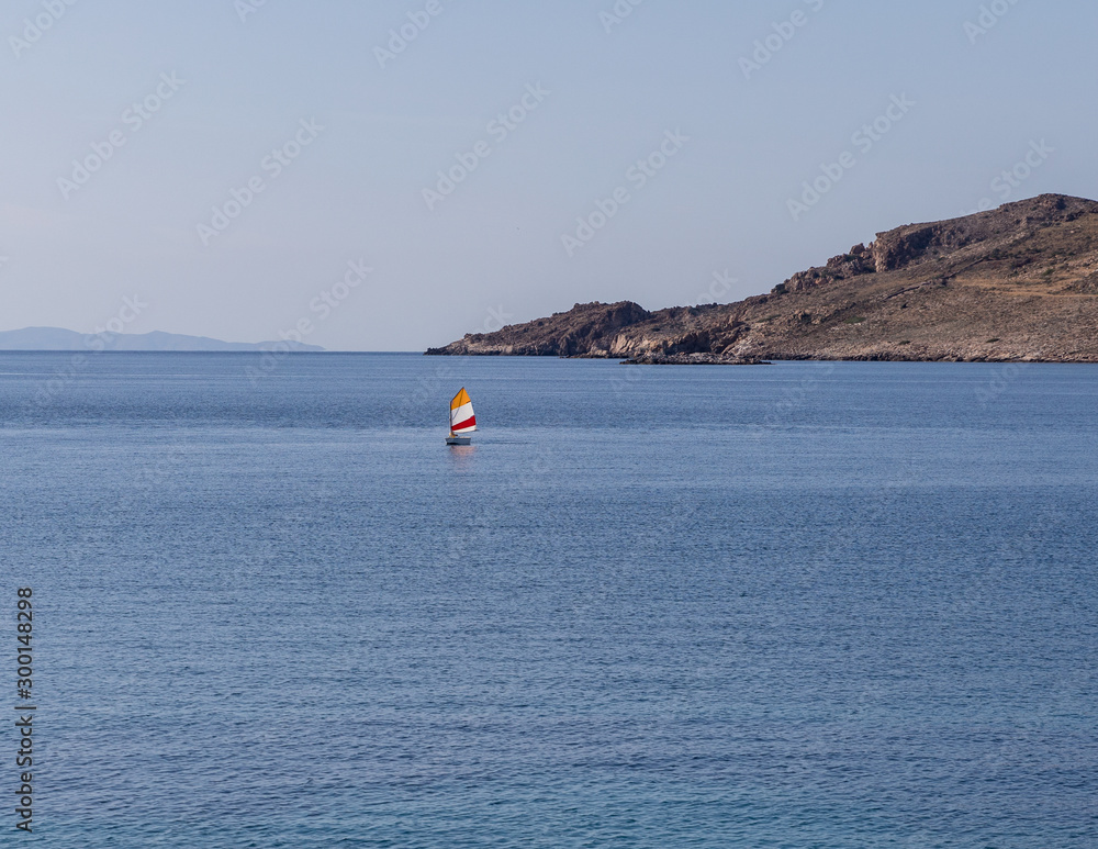 Single dinghy sailing boat in the blue Aegean Sea.