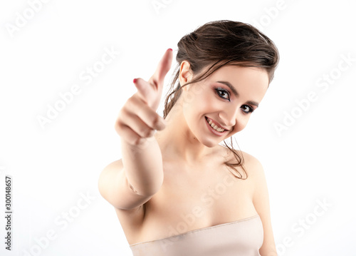 A beautiful smiling brunette girl with bare shoulders points her finger forward. Isolated on white. Advertising and commercial design. Copy space.