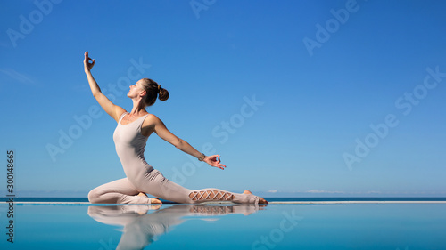 Beautiful young woman doing homukhasana sitting on the edge of the pool against the blue sky while relaxing on the beach. The concept of opening the chest and aligning the back. Copyspace 16:9