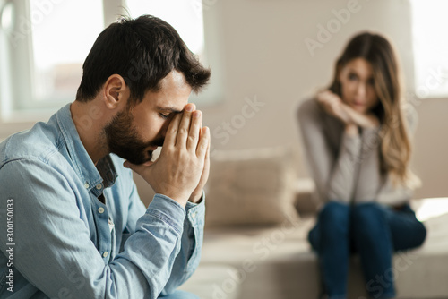 Young man feeling sad after arguing with his girlfriend on sofa at home