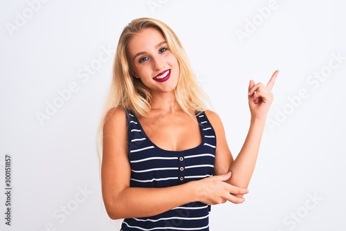 Young beautiful woman wearing casual striped t-shirt standing over isolated white background with a big smile on face, pointing with hand and finger to the side looking at the camera.