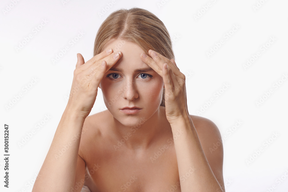 Portrait of a sexy blond caucasian young woman looking in the mirror, observing facial wrinkles, first sign of aging Portrait of a sexy blond caucasian young woman looking in the mirror, observing facial wrinkles, first sign of aging