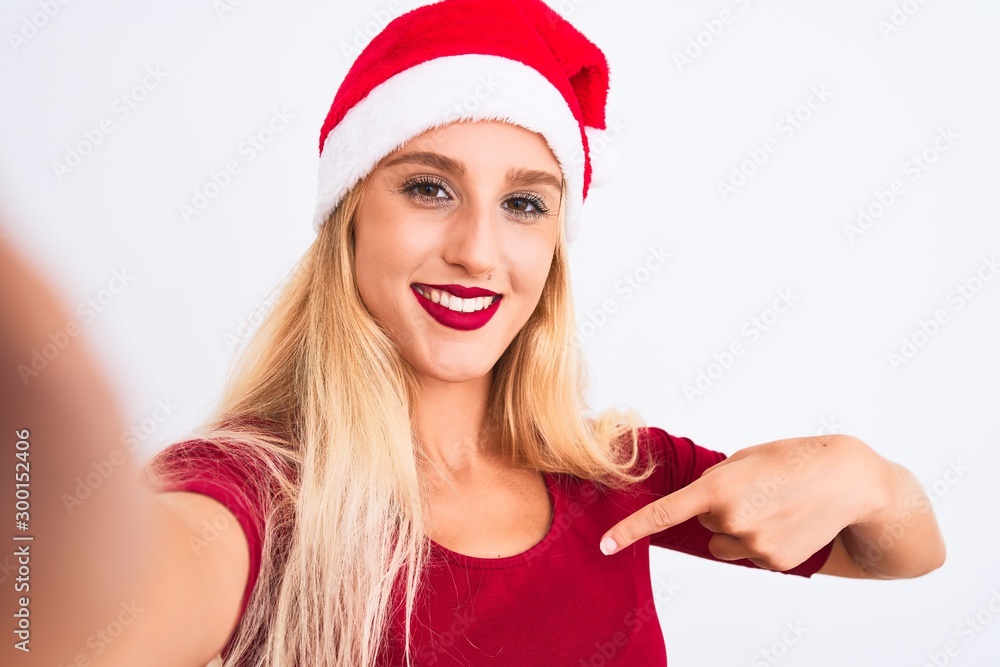 Woman wearing Christmas Santa hat make selfie by camera over isolated white background with surprise face pointing finger to himself Woman wearing Christmas Santa hat make selfie by camera over isolated white background with surprise face pointing finger to himself