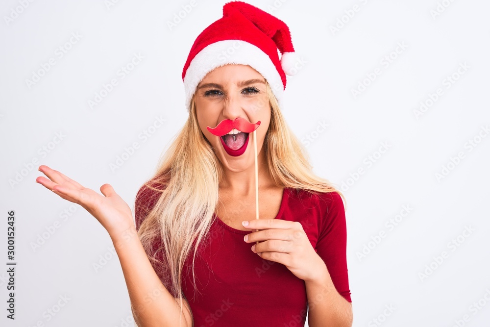 Woman wearing Christmas Santa hat holding fanny mustache over isolated white background very happy and excited, winner expression celebrating victory screaming with big smile and raised hands Woman wearing Christmas Santa hat holding fanny mustache over isolated white background very happy and excited, winner expression celebrating victory screaming with big smile and raised hands