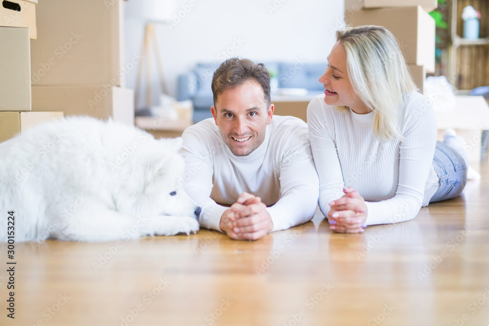 Young beautiful couple with dog lying down on the floor at new home around cardboard boxes Young beautiful couple with dog lying down on the floor at new home around cardboard boxes