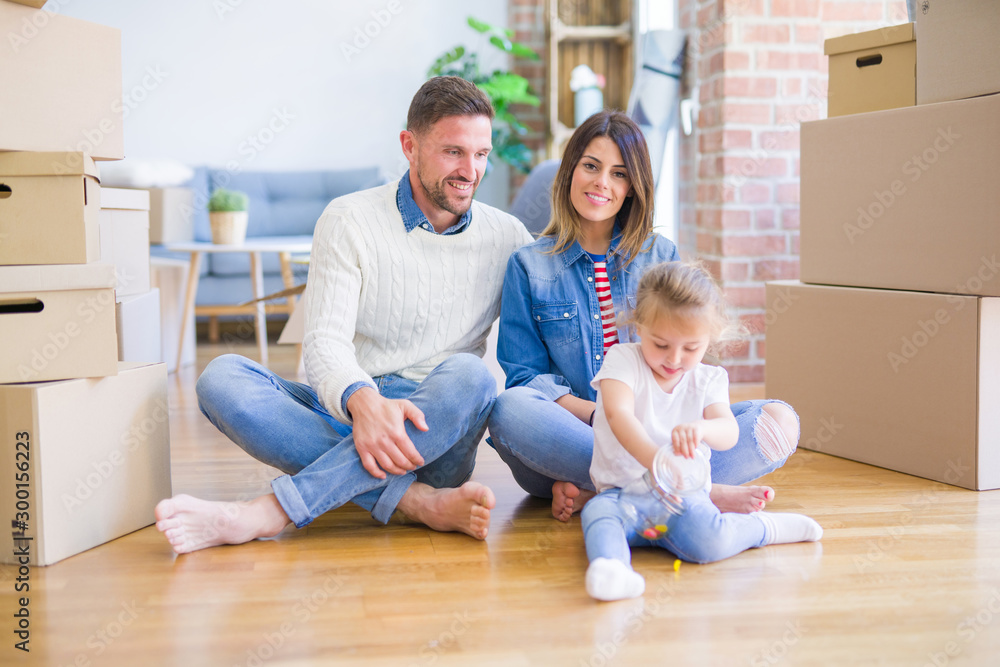 Beautiful family sitting on the floor playing with his kid at new home around cardboard boxes