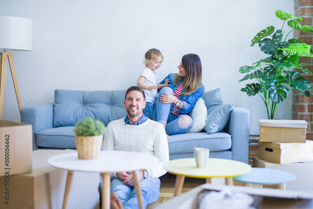 Beautiful family, parents sitting on the sofa looking his kid jumping at new home around cardboard boxes Beautiful family, parents sitting on the sofa looking his kid jumping at new home around cardboard boxes