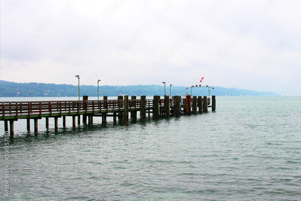 Long pier with flag off blue water in Lindau Germany mountain hill background