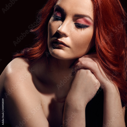Fashionable portrait of beautiful redheaded model with naked shoulders on black background