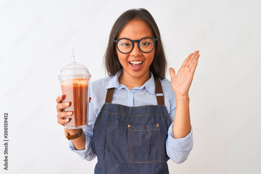 Chinese woman wearing glasses apron drinking smoothie over isolated white background very happy and excited, winner expression celebrating victory screaming with big smile and raised hands Chinese woman wearing glasses apron drinking smoothie over isolated white background very happy and excited, winner expression celebrating victory screaming with big smile and raised hands