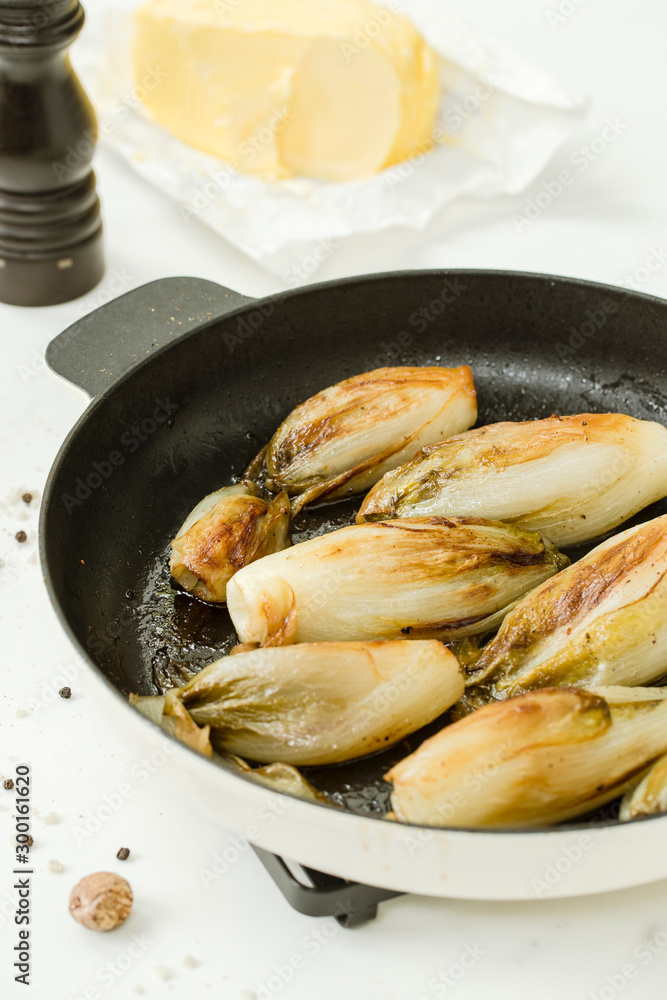 Braised chicory on the belgian way in a baking pan with butter and pepper grinder Braised chicory on the belgian way in a baking pan with butter and pepper grinder