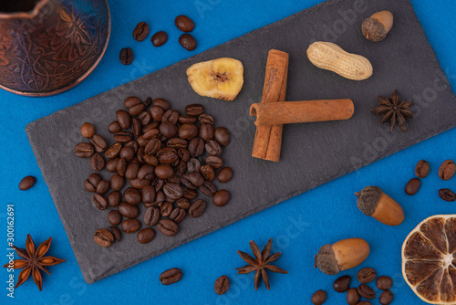 Beautiful composition of coffee beans, utensils for making coffee and decor in the form of almonds, dried slices of lemon, peanut and cinnamon on black and blue backgrounds.