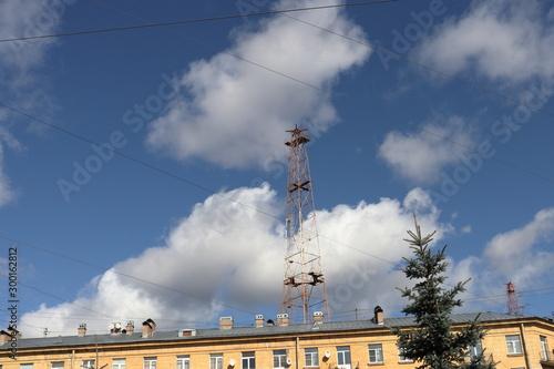 Abandoned old radio tower behind a residential building against a bright blue sky with fluffy clouds