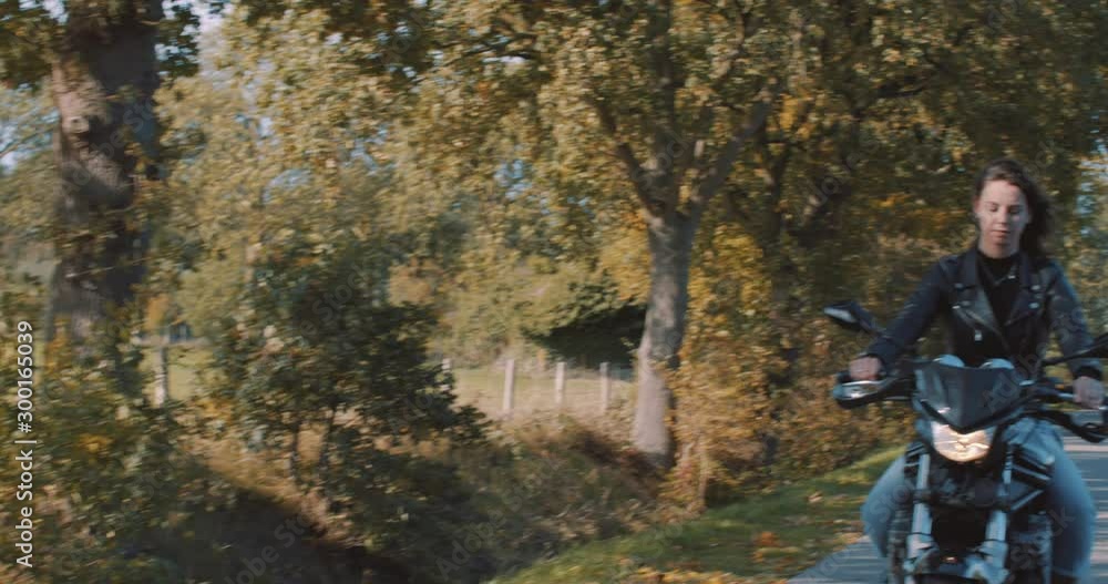 Beautiful smiling European Female motor Biker wearing leather jacket driving On road panning to field with autumn leaf colored Trees in forest on sunny day. Slow Motion in Utrecht, Netherlands Beautiful smiling European Female motor Biker wearing leather jacket driving On road panning to field with autumn leaf colored Trees in forest on sunny day. Slow Motion in Utrecht, Netherlands