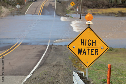 High water warning sign with floodwater crossing the road near Albany, Oregon.