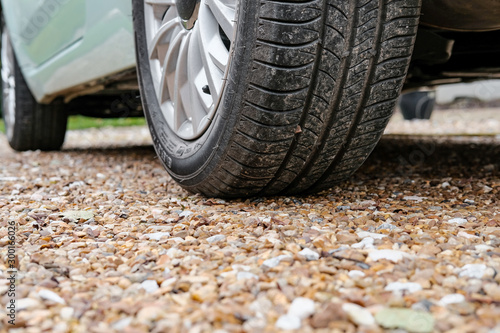 Ground level view of a new car, showing the rear tyre and tread together with the alloy wheel. Parked on a gravel driveway and showing some of its light blue paint. photo
