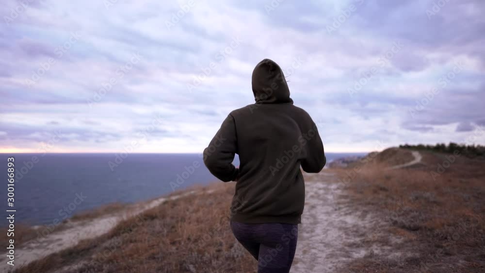 One woman jogging on a cliff at dusk. Sportswoman in a sweatshirt during an outdoor running training One woman jogging on a cliff at dusk. Sportswoman in a sweatshirt during an outdoor running training