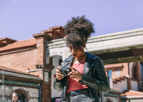 Attractive brunette tourist woman with afro hair checks her vintage camera before taking a picture of the city