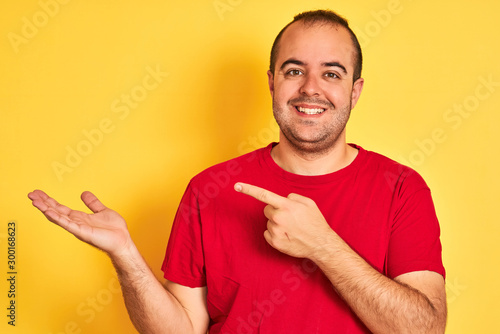 Young man wearing red casual t-shirt standing over isolated yellow background very happy pointing with hand and finger
